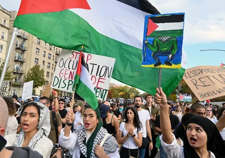 Pro-Palestine protesters holding Palestinian flags and signs during a large demonstration calling for ceasefire and human rights protections.