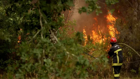 Aerial view of massive wildfires burning through forests in southwestern France and Spain in July 2026, with thick smoke rising over residential areas