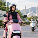 A Pakistani woman wearing a safety helmet riding an electric scooter on an urban road.